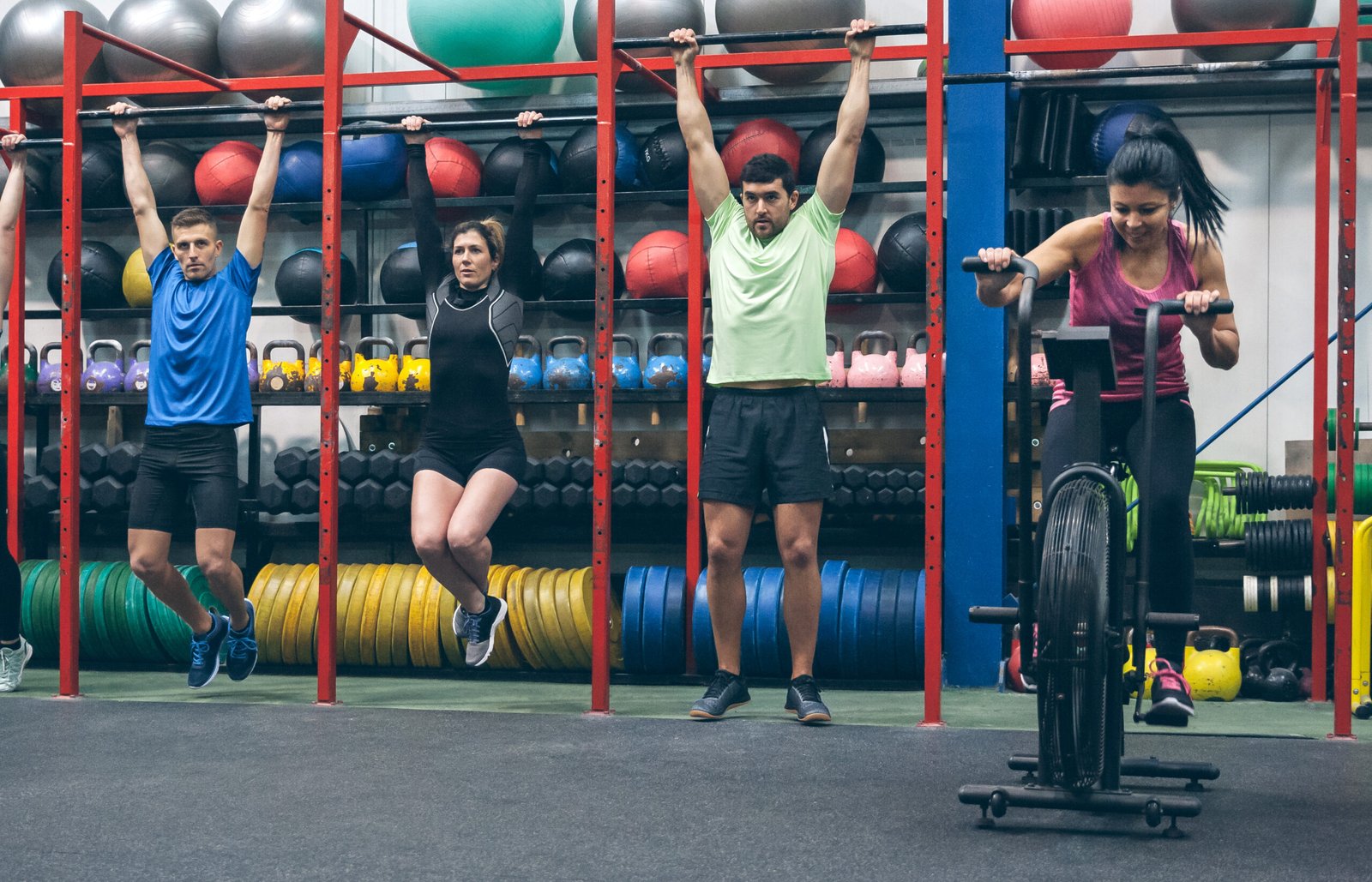 Atletas haciendo pull-ups y air bike en el gimnasio, ideal para un box de crossfit en Mataró